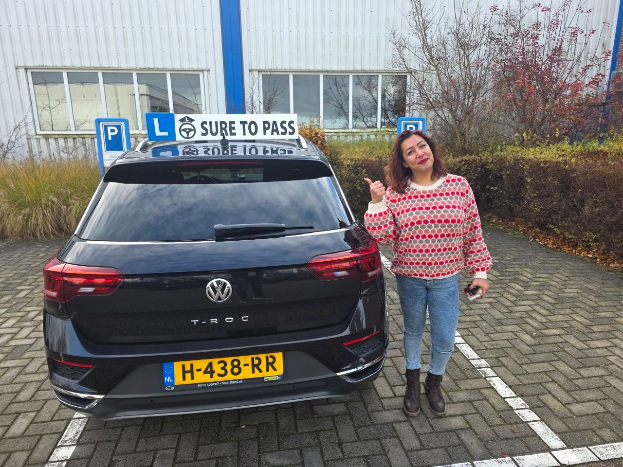 Geslaagde leerling steekt haar duim op naast de zwarte lesauto van Sure to Pass