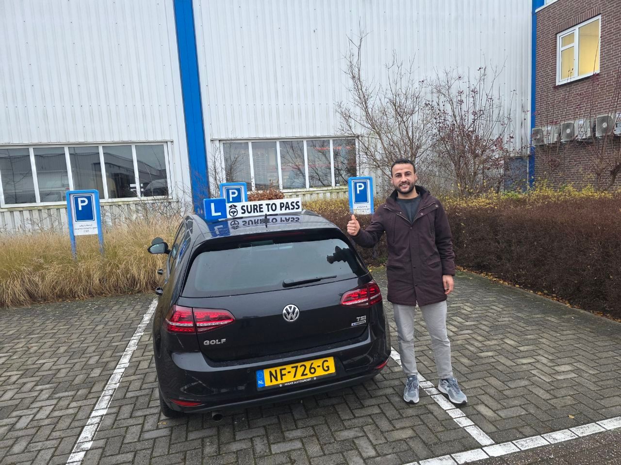 Geslaagde leerling wijst naar het L-bord op de lesauto van Sure to Pass