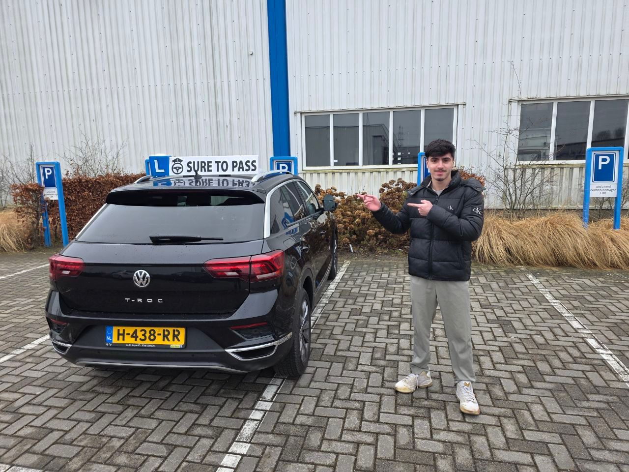 Geslaagde leerling houdt zijn autosleutel omhoog naast de lesauto