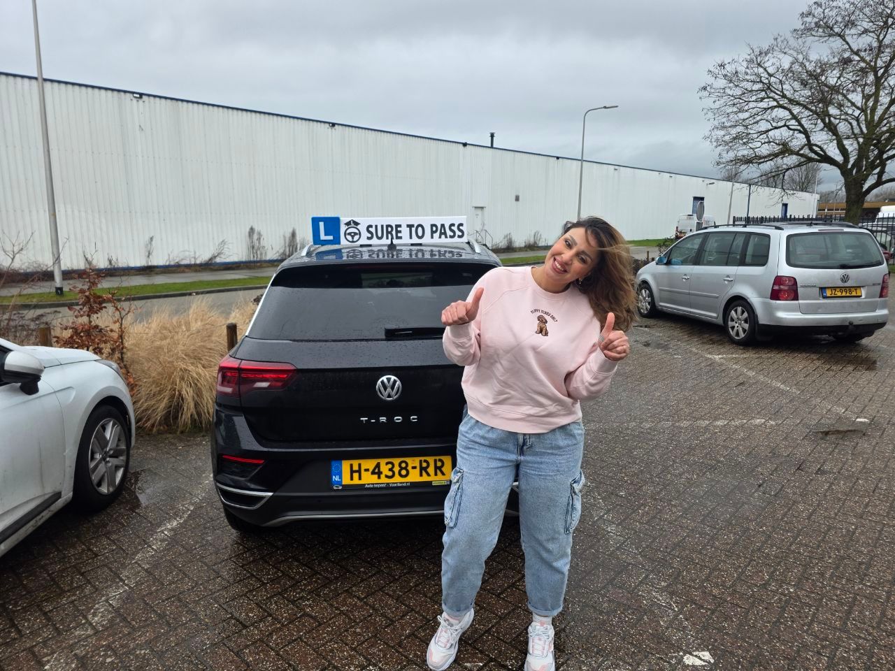 Geslaagde leerling lacht naar de camera naast de lesauto van Sure to Pass