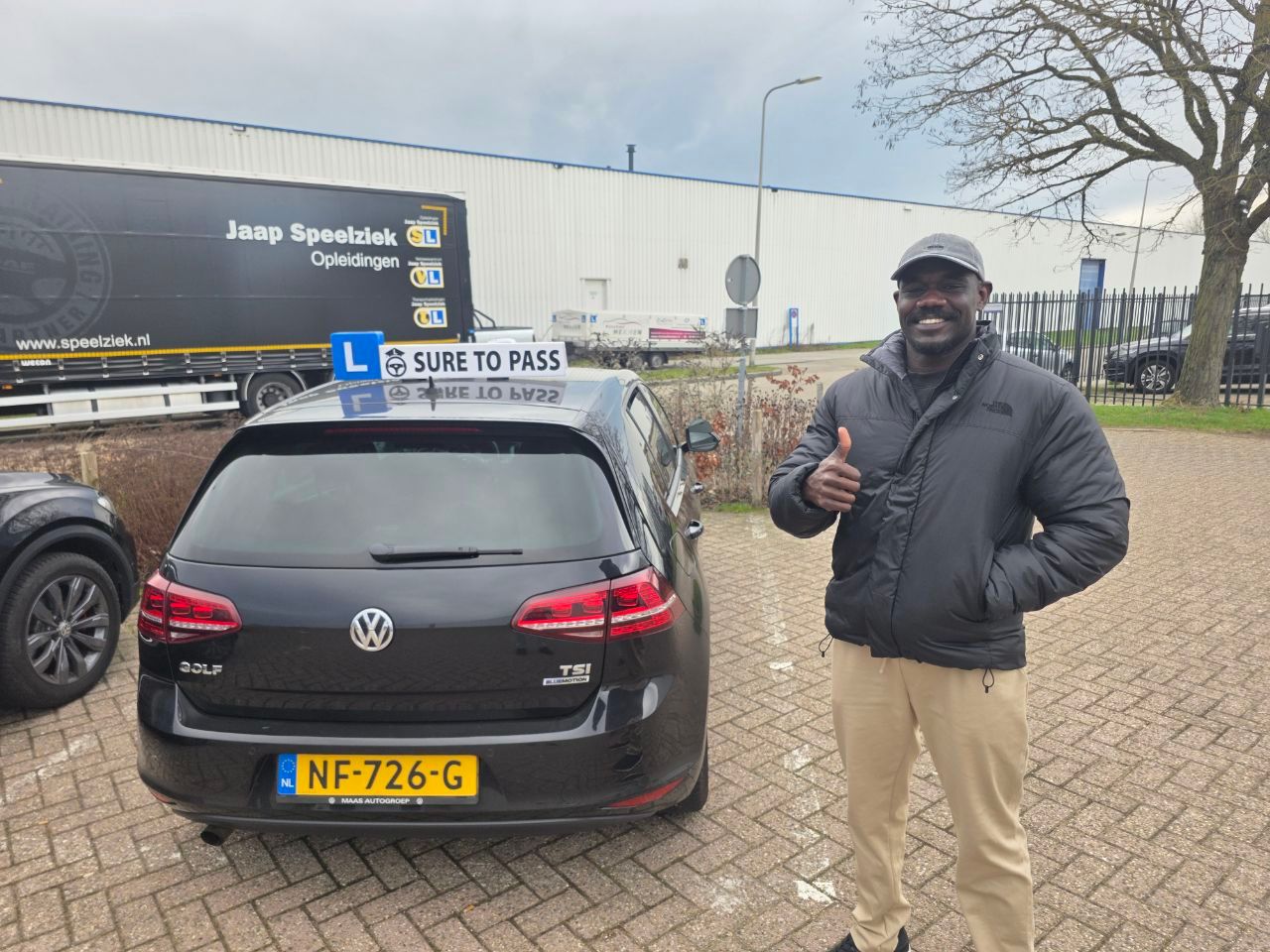 Geslaagde leerling met opgestoken duim naast de donkere Volkswagen Golf van de rijschool
