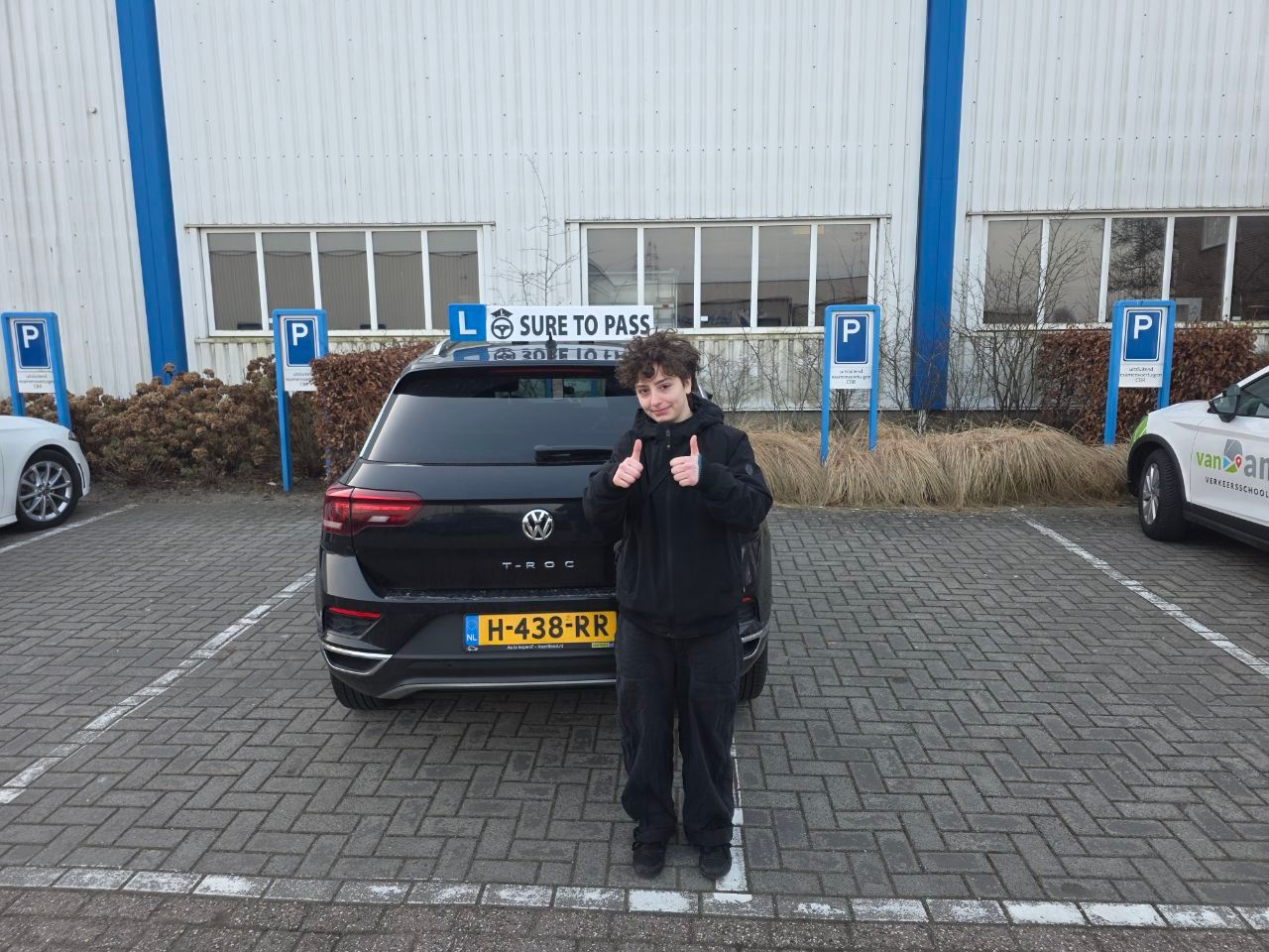 Geslaagde leerling steekt beide duimen op bij de lesauto