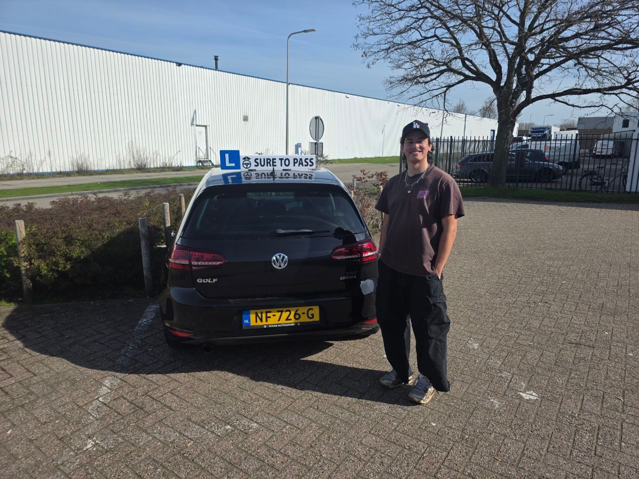 Geslaagde leerling met pet naast de lesauto van Sure to Pass